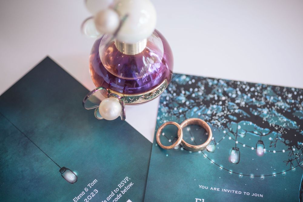 Wedding rings and purple perfume bottle displayed on a teal book with sparkly decorative background.