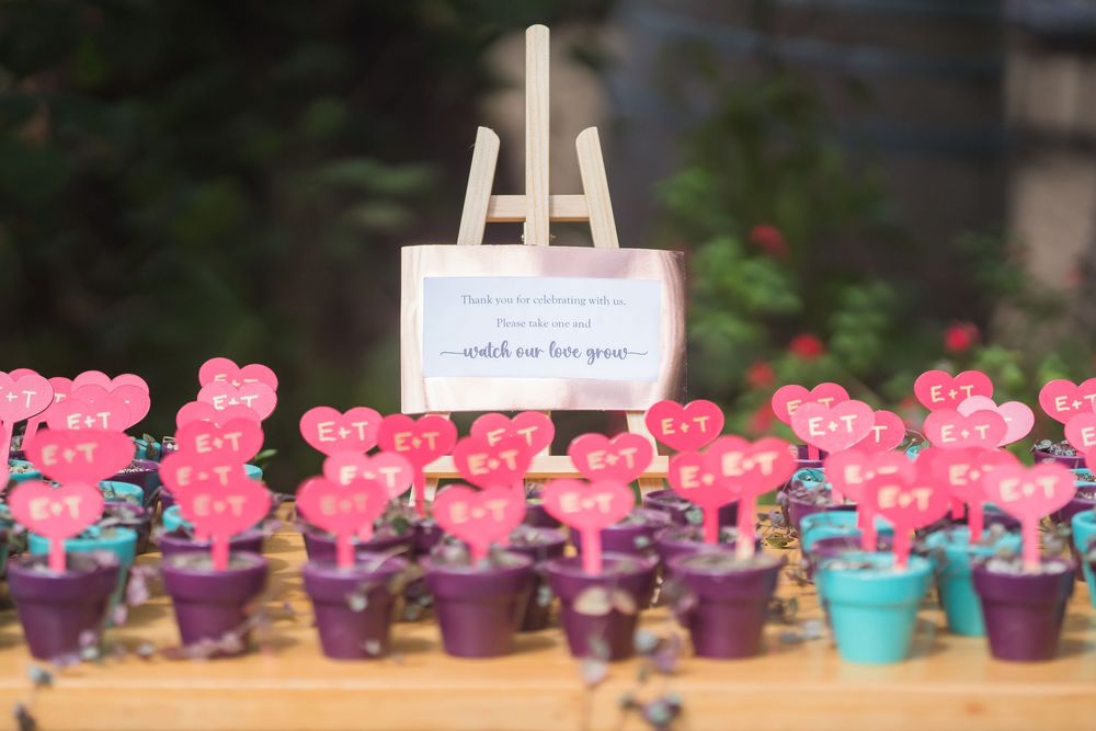 Small pink teddy bear party favors arranged in colorful mini pots with a white display easel in the background.