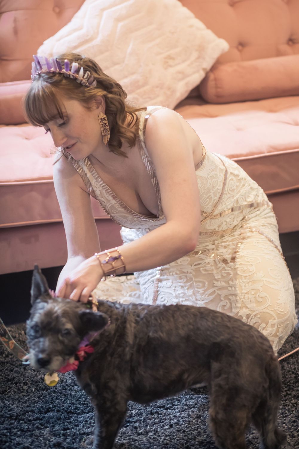 A person in a white lace dress pets a large dark-colored dog on a black carpet.