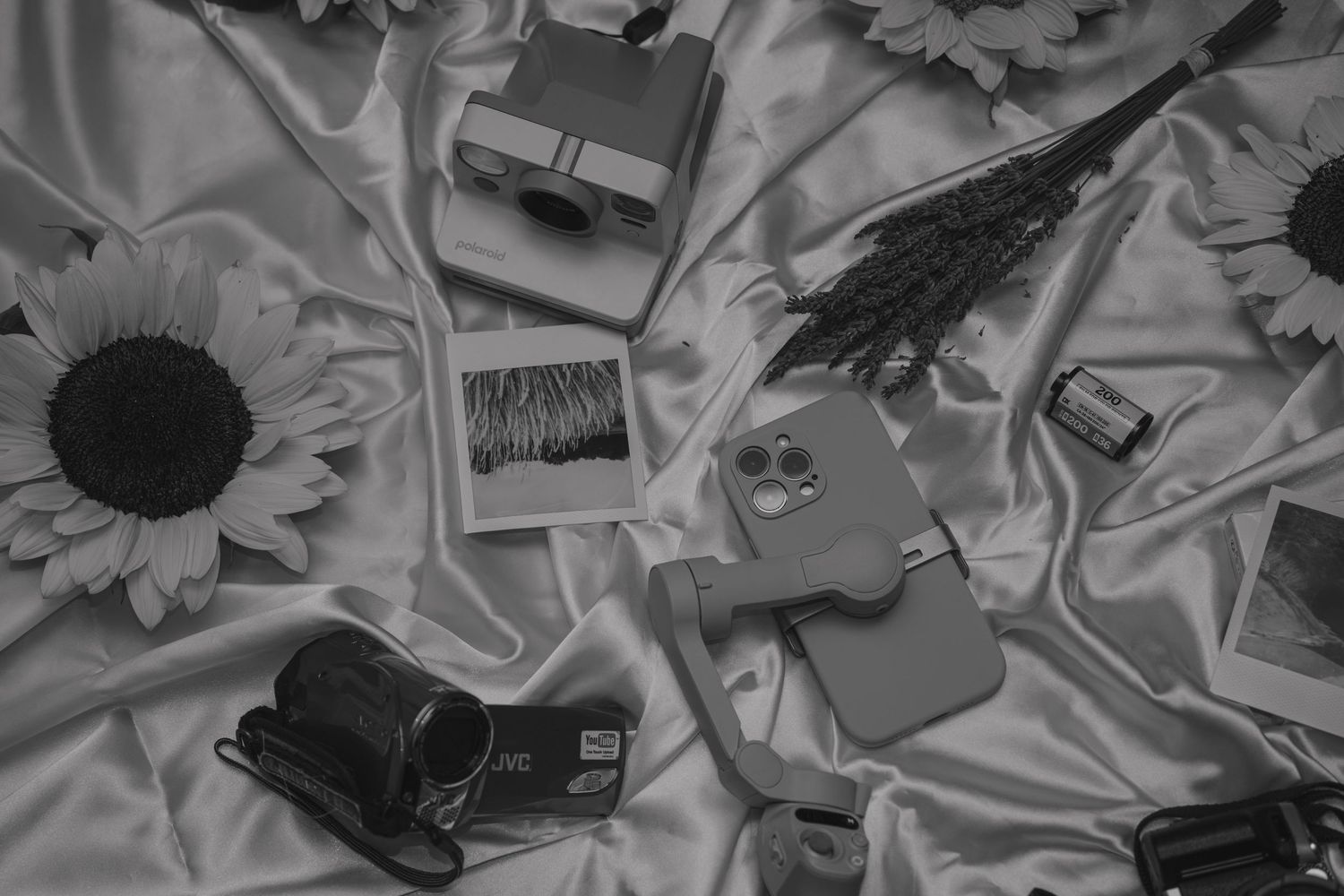 Black and white flatlay of vintage cameras, polaroids and sunflowers on fabric.