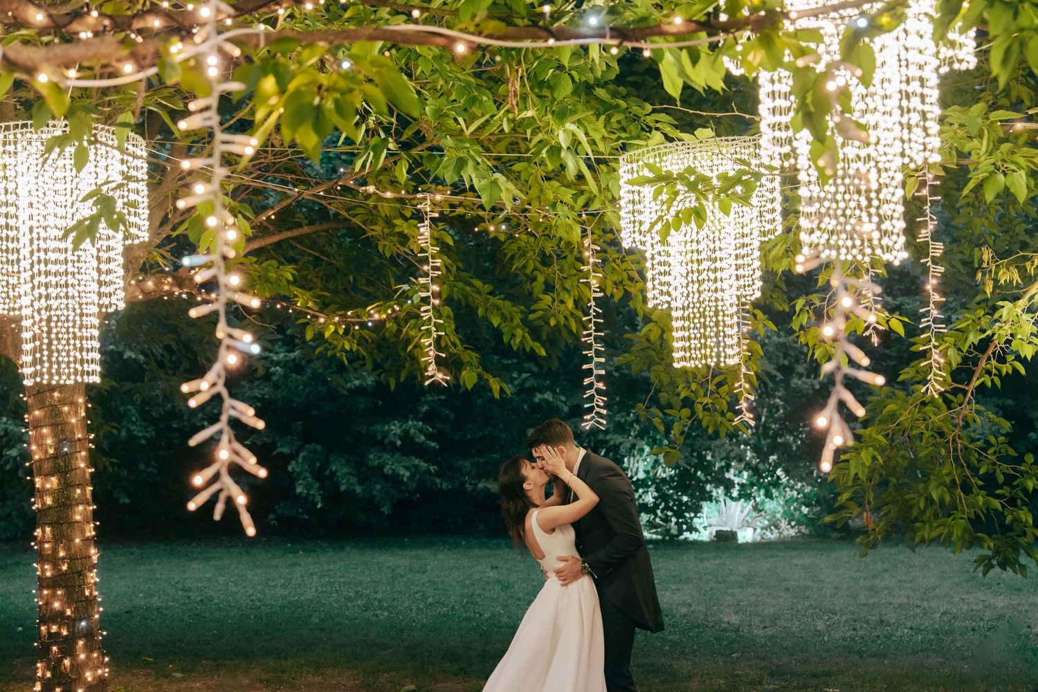 Una coppia romantica di sposi durante il loro matrimonio mentre si baciano sotto le luci e gli alberi alla location Locanda La Valle