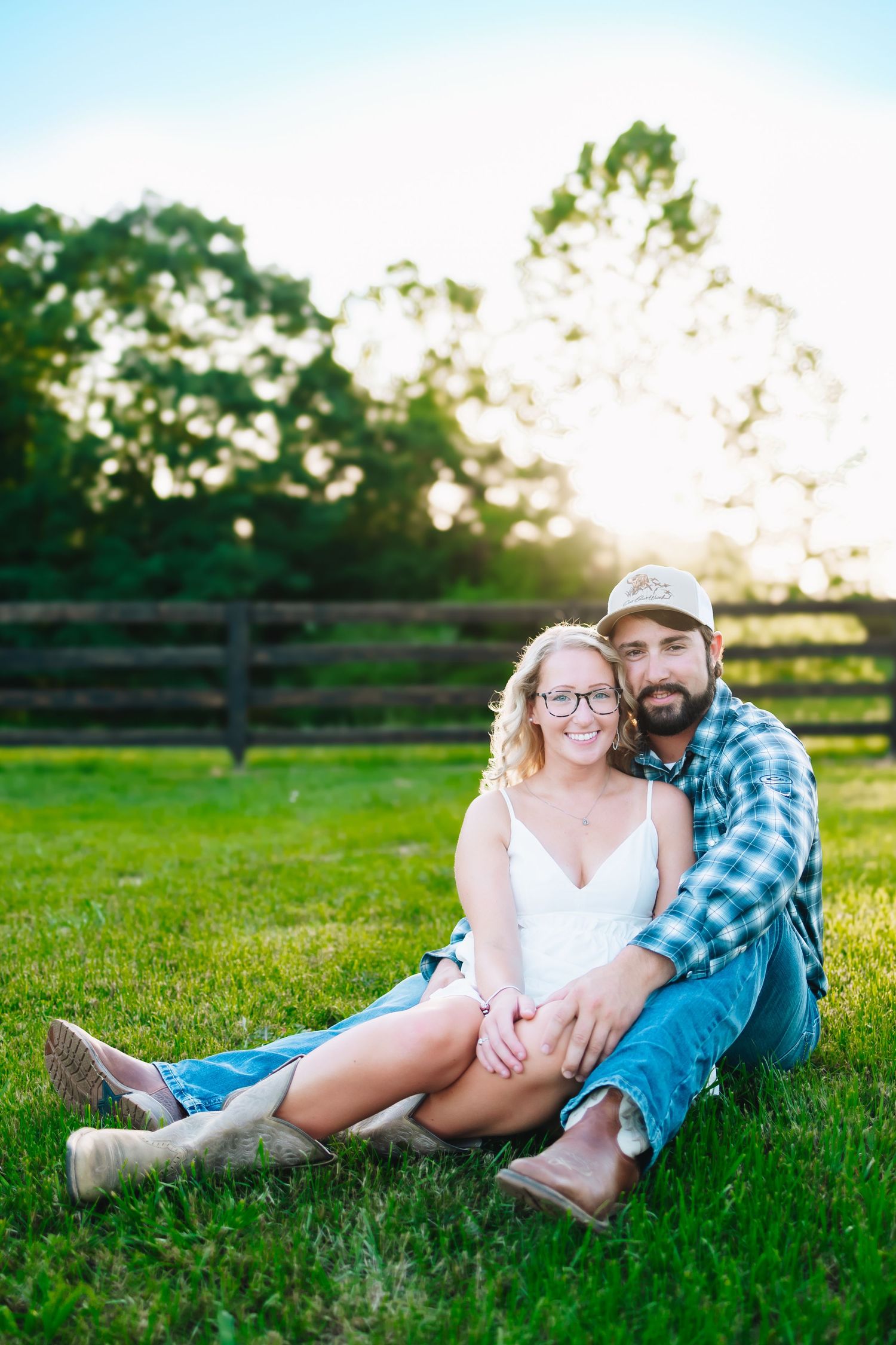 Couple relaxes together on green grass during golden hour engagement session.