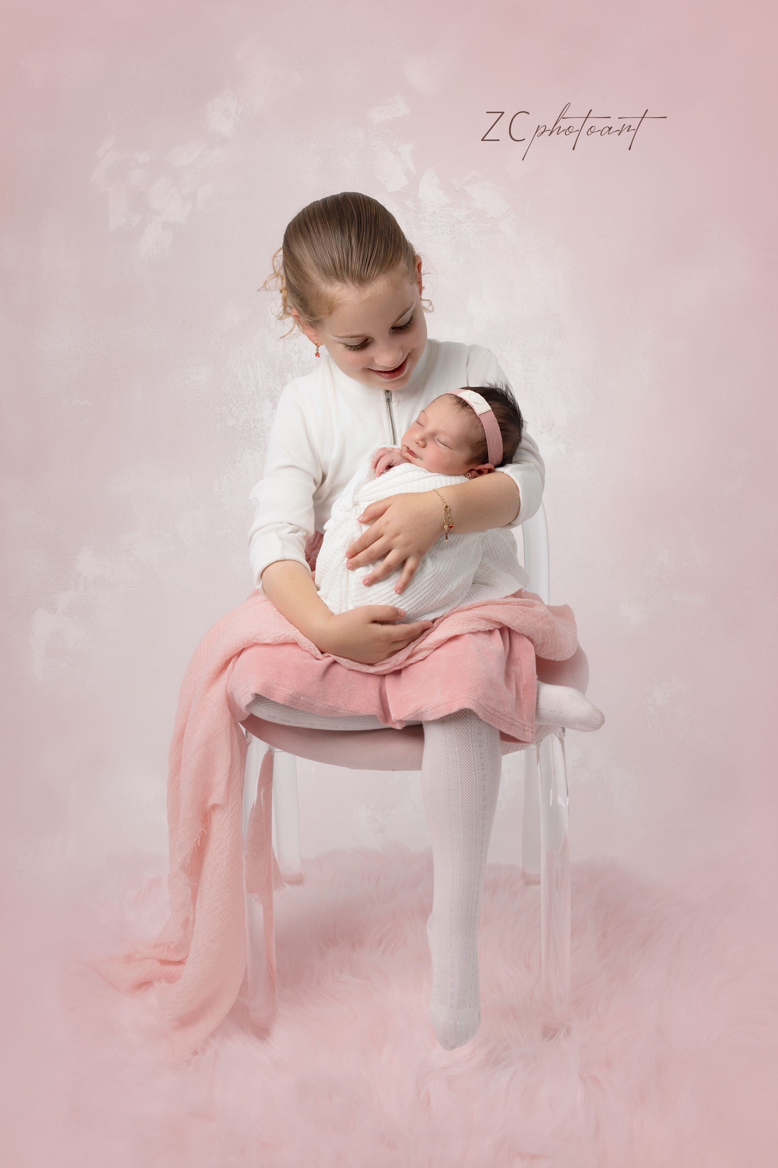 Sweet portrait of siblings on a white chair against pink backdrop with delicate fabric draping.