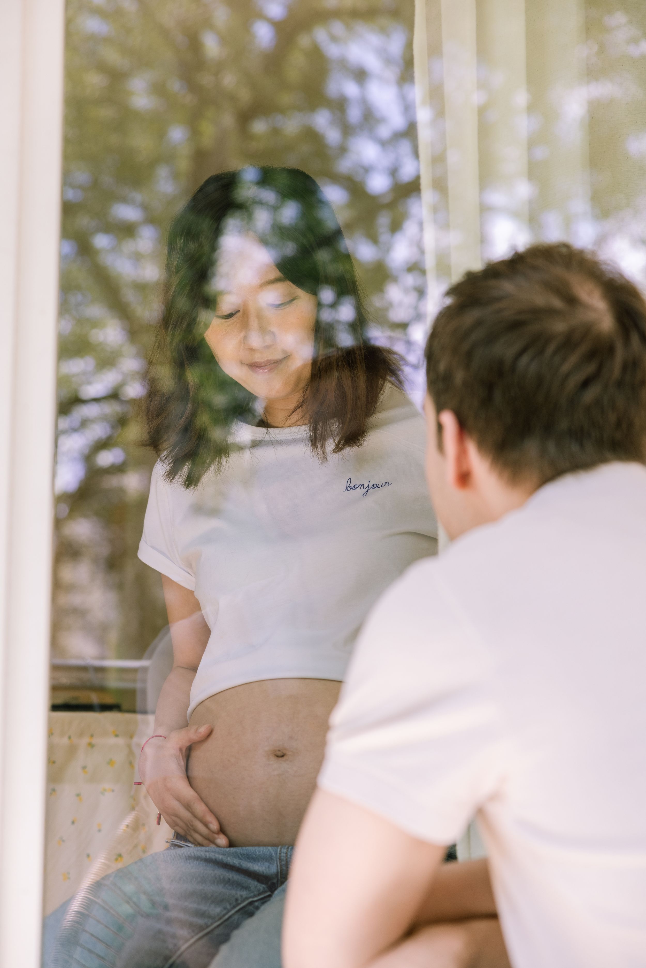 Maternity photo captured through window reflection with soft natural light.