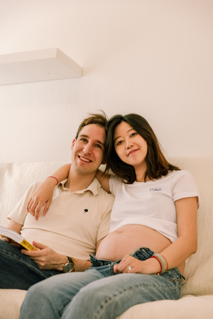 Expecting couple relaxes together on white couch during pregnancy photoshoot.