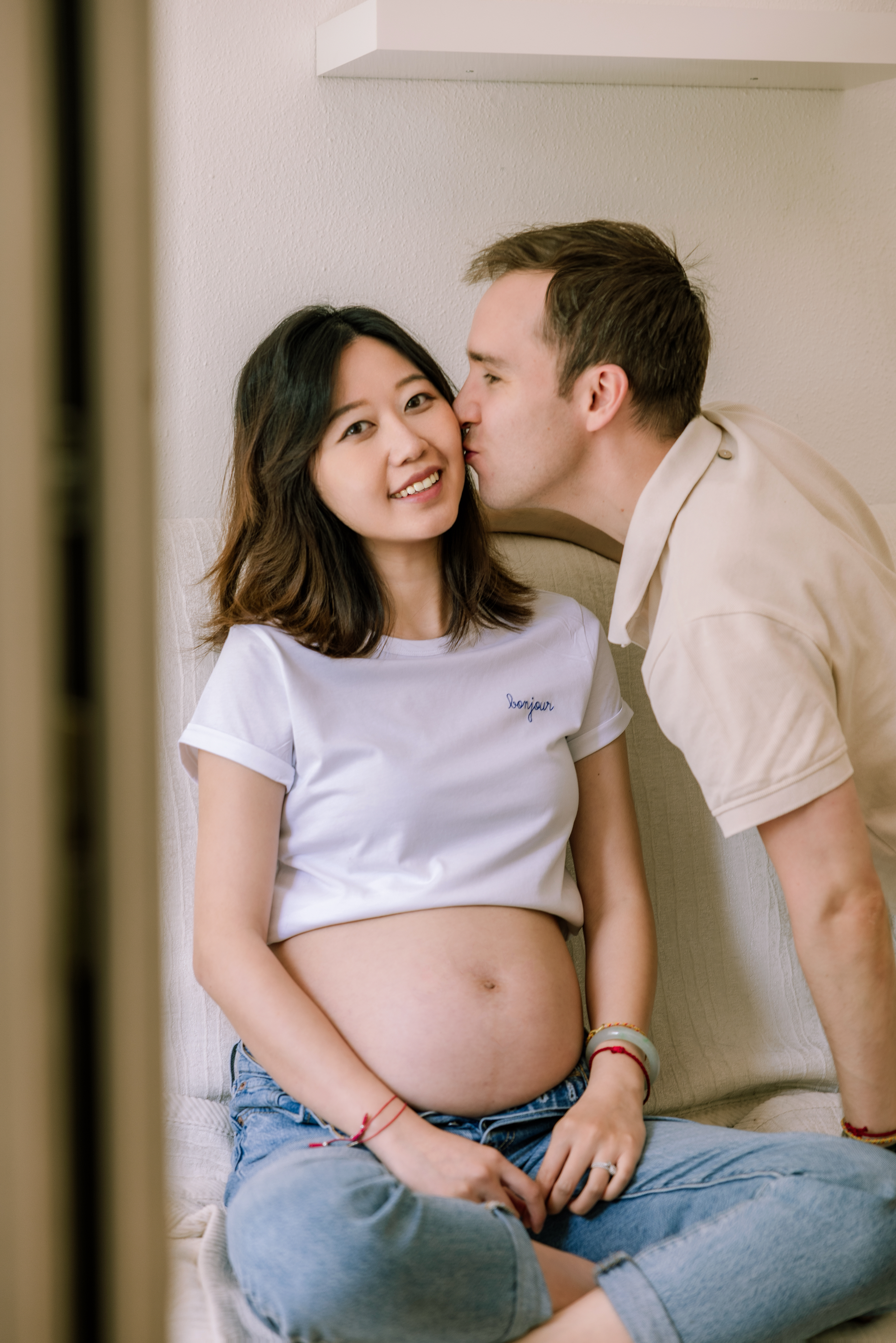 Intimate moment between couple during pregnancy photoshoot against white wall.