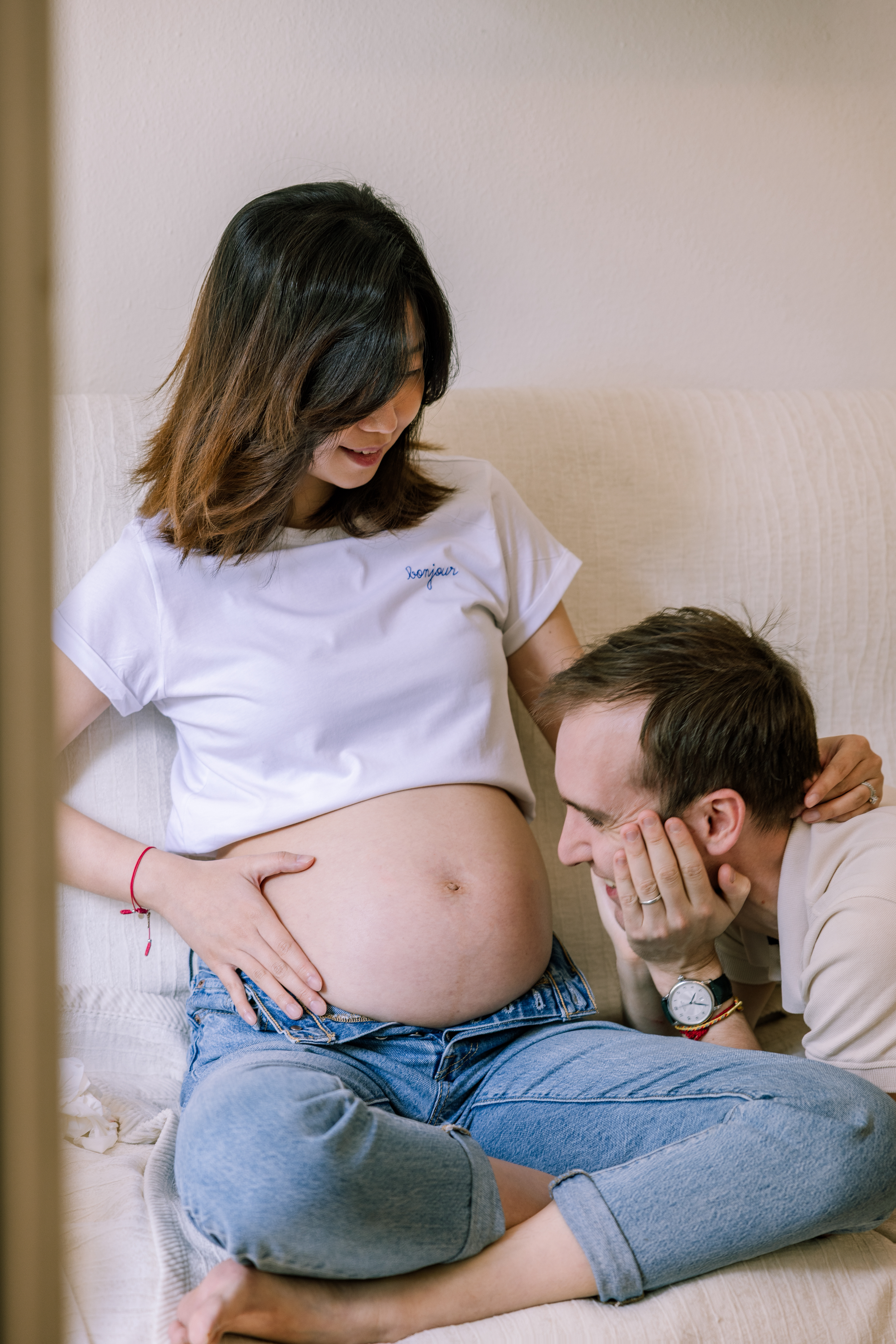 Tender maternity moment captured as couple sits on white couch.
