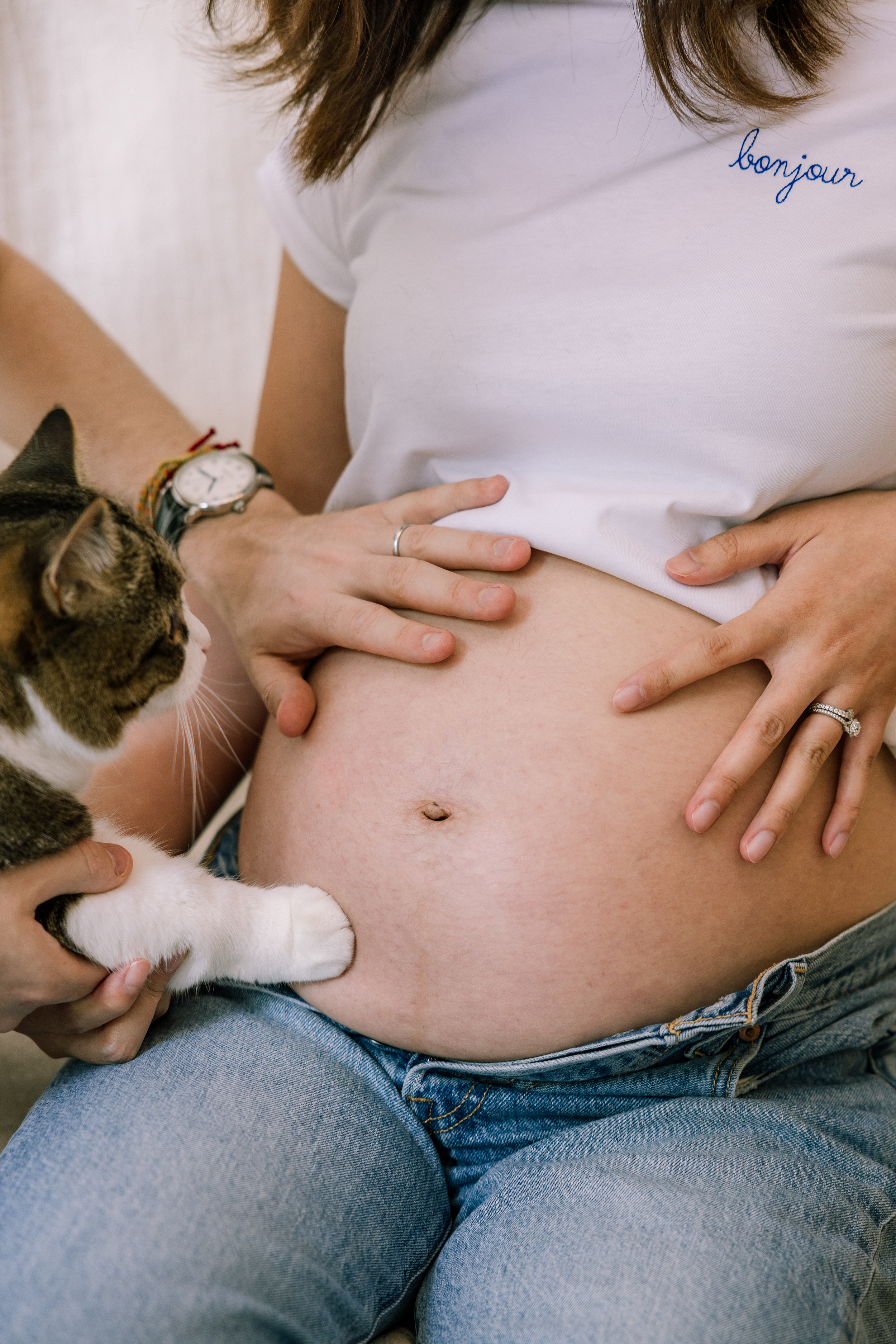 Cat rests paw on pregnant belly visible beneath white t-shirt and jeans.