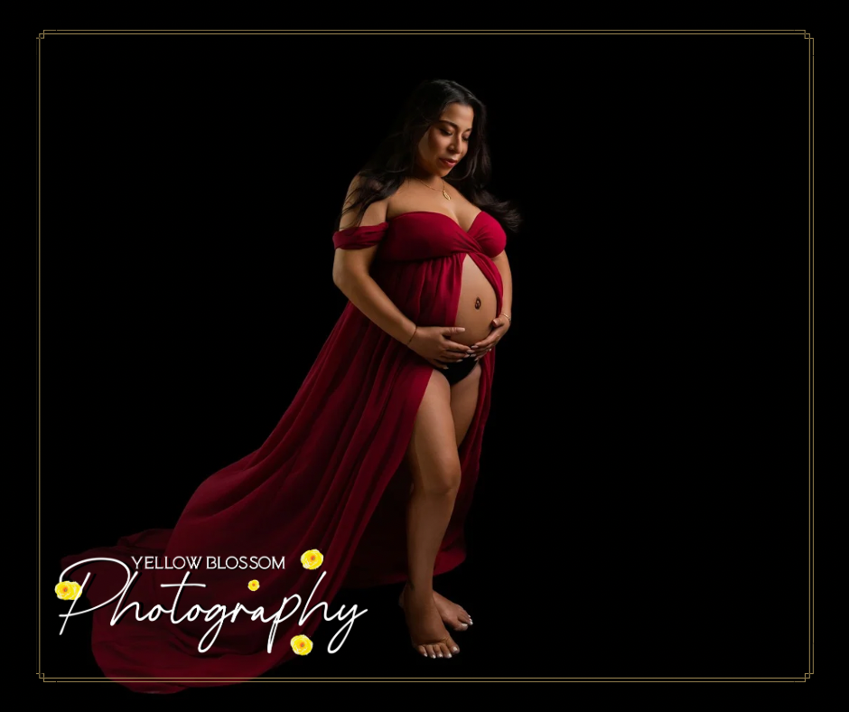 Elegant maternity portrait featuring a dramatic red off-shoulder gown against a dark background with gold text overlay.