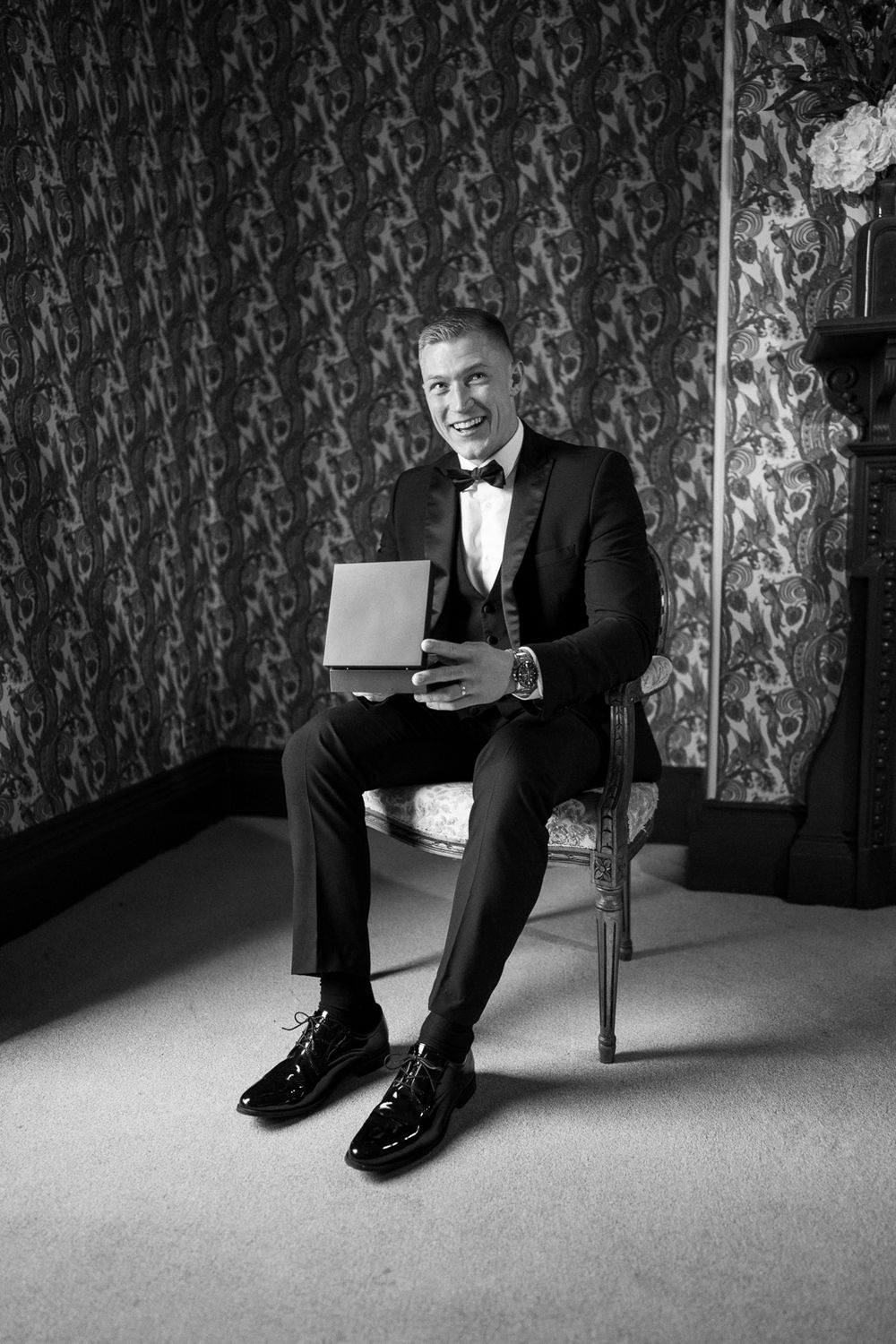 Black and white sequence of close-up shots showing polished dress shoes and suit pants against decorative wallpaper.