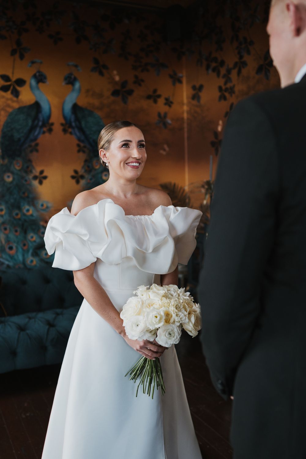 A romantic wedding day moment captured with a white bouquet of flowers in an elegant room with floral wallpaper.