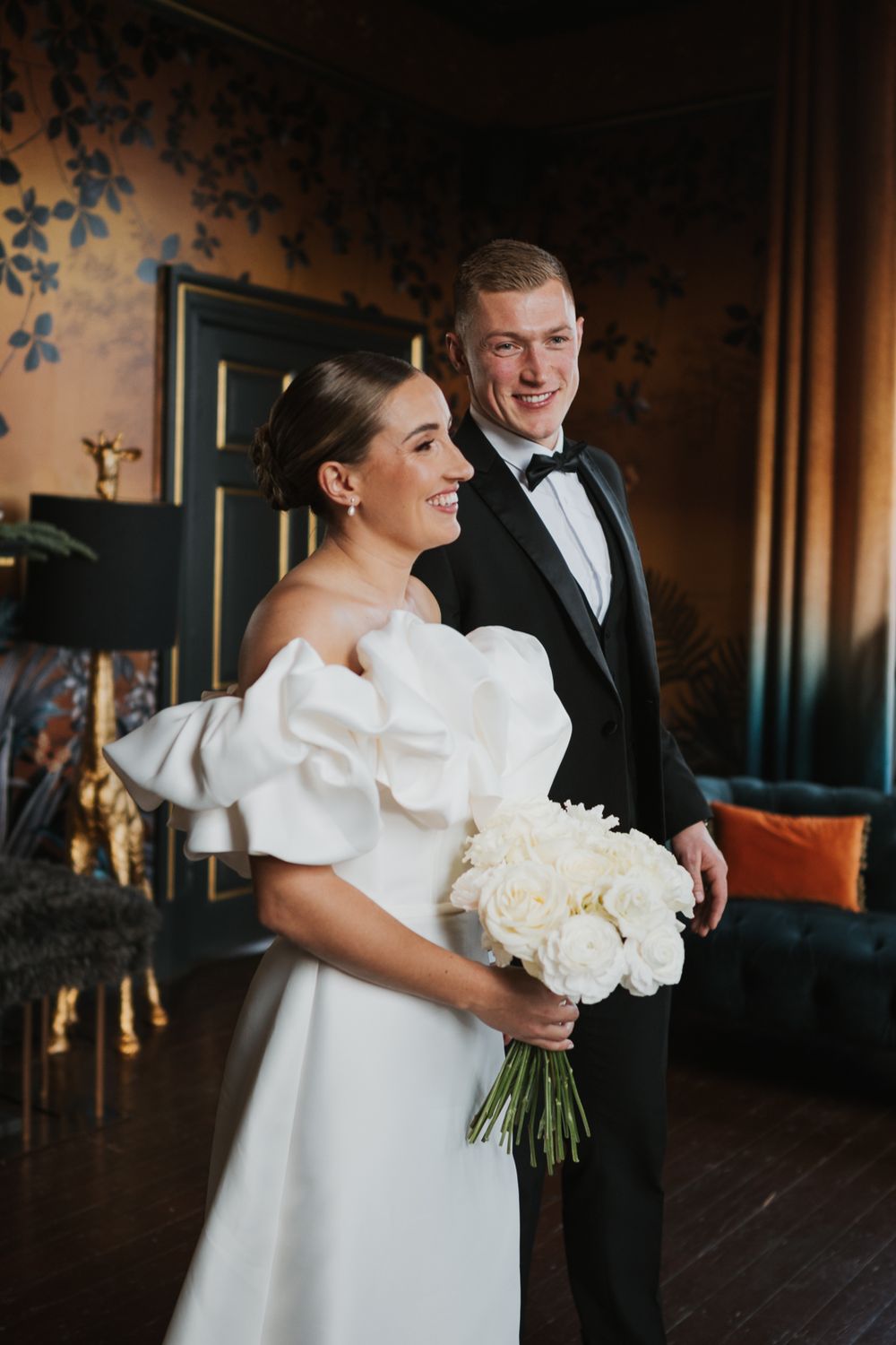 Bride in elegant white wedding gown with dramatic puff sleeves holds classic white bouquet in opulent indoor setting.