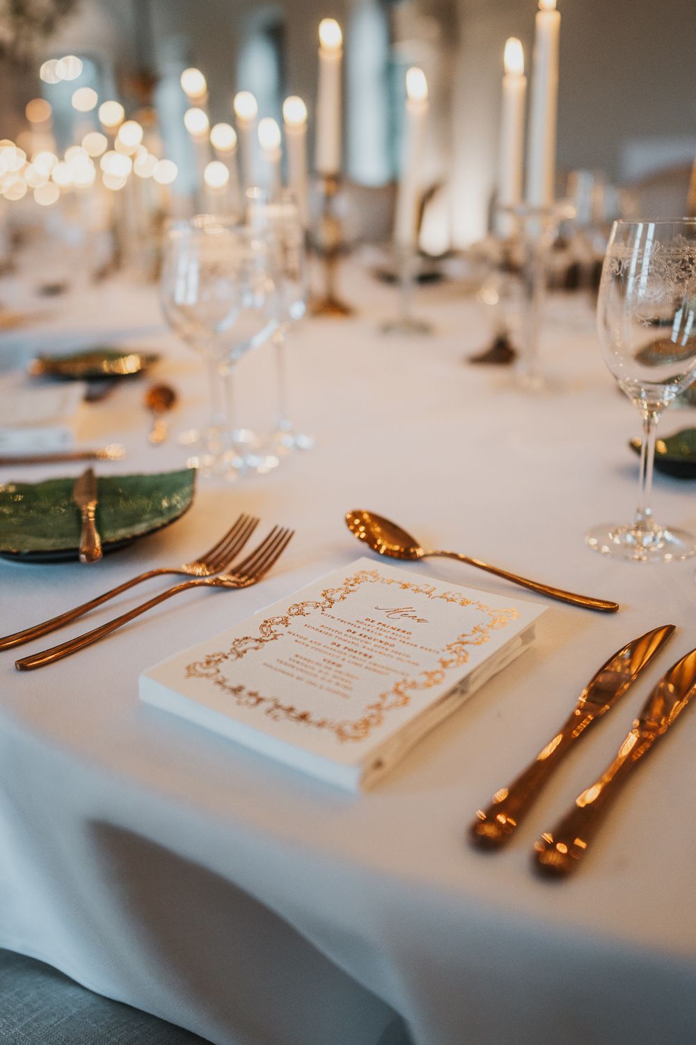 Close-up of formal place setting with gold utensils, menu card and white tablecloth at wedding reception.