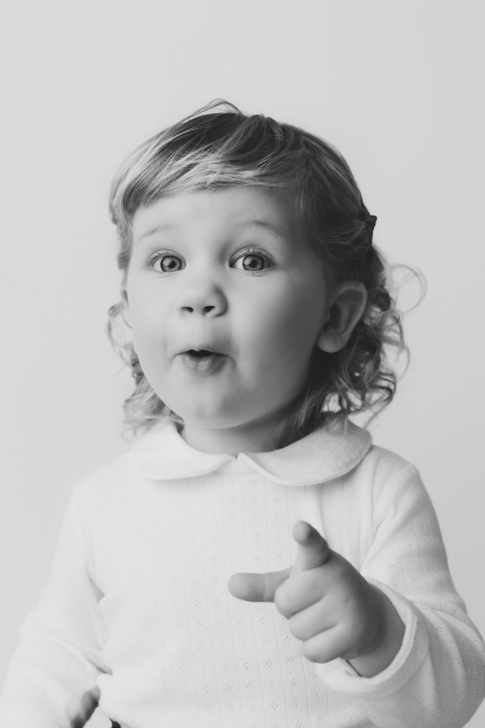 Black and white portrait of a cute toddler with curly hair pointing finger, making a funny surprised expression.