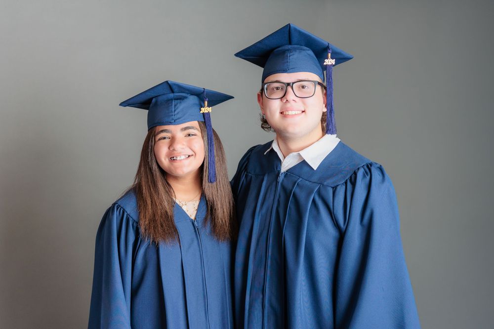 Two smiling graduates in blue caps and gowns posing together for a graduation portrait photo.
