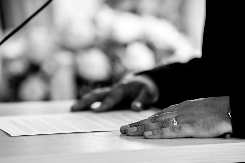 Black and white photo of hands resting on a document at a signing ceremony, one hand wearing a ring.