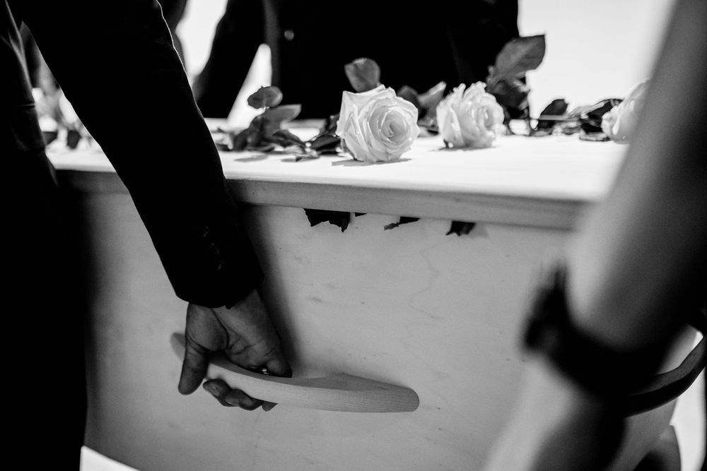 Black and white photo of pallbearers carrying a white casket adorned with white roses at a funeral.