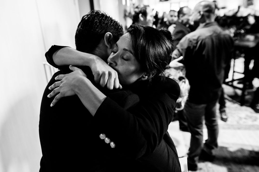 Black and white photo of a couple sharing a tender embrace and kiss at a social gathering.