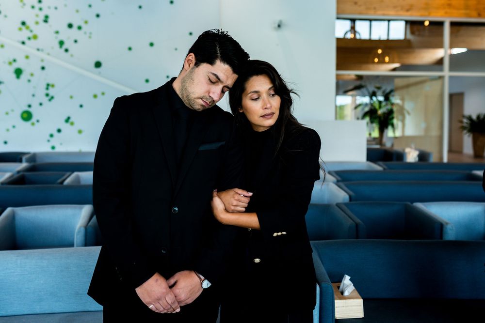 Couple dressed in black embracing in a modern interior space, sharing a tender emotional moment.