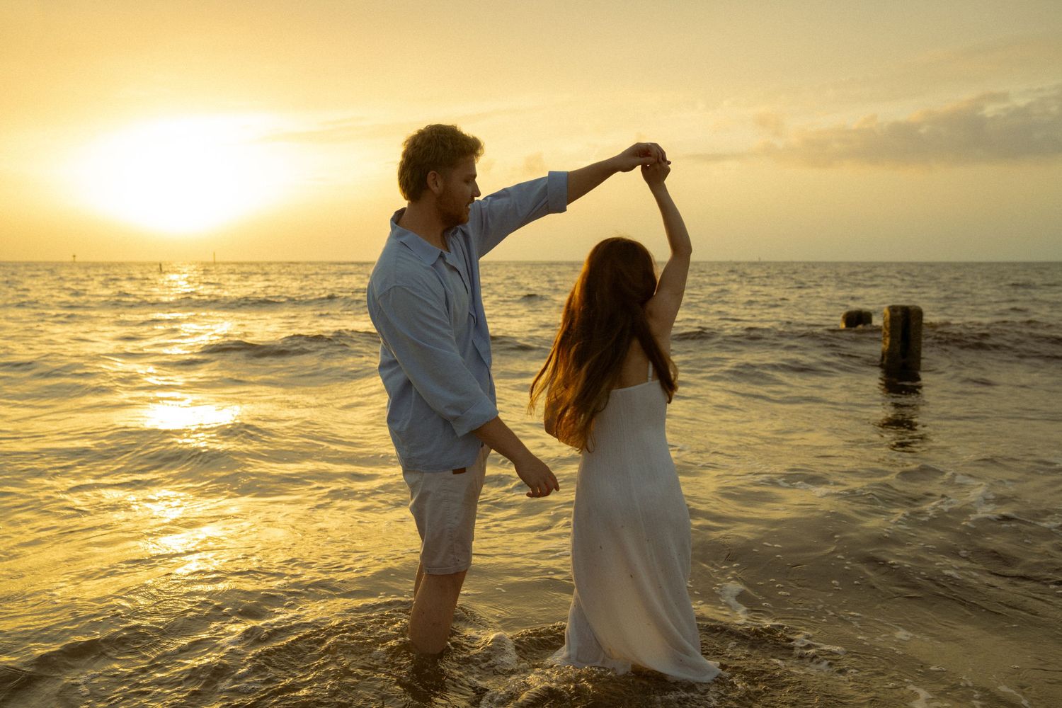 Couple dancing romantically in ocean waves at golden sunset on tropical beach.