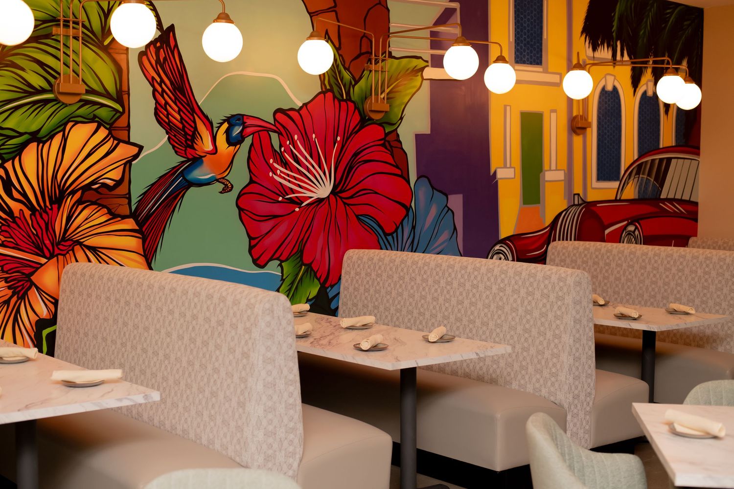 Colorful tropical mural with hibiscus flowers and a hummingbird decorates a restaurant dining room.