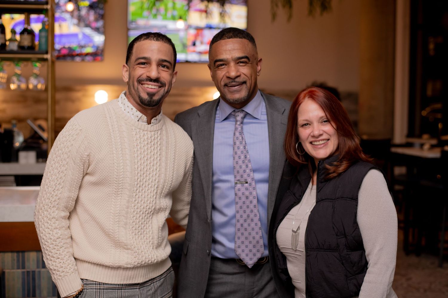 Three people smile together in a warmly lit restaurant during a casual social gathering.