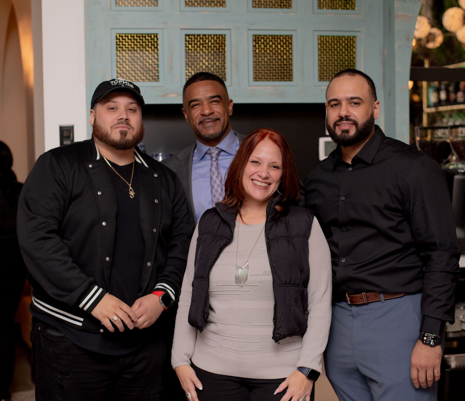 Four people smile together posing in front of a decorative door at a restaurant.