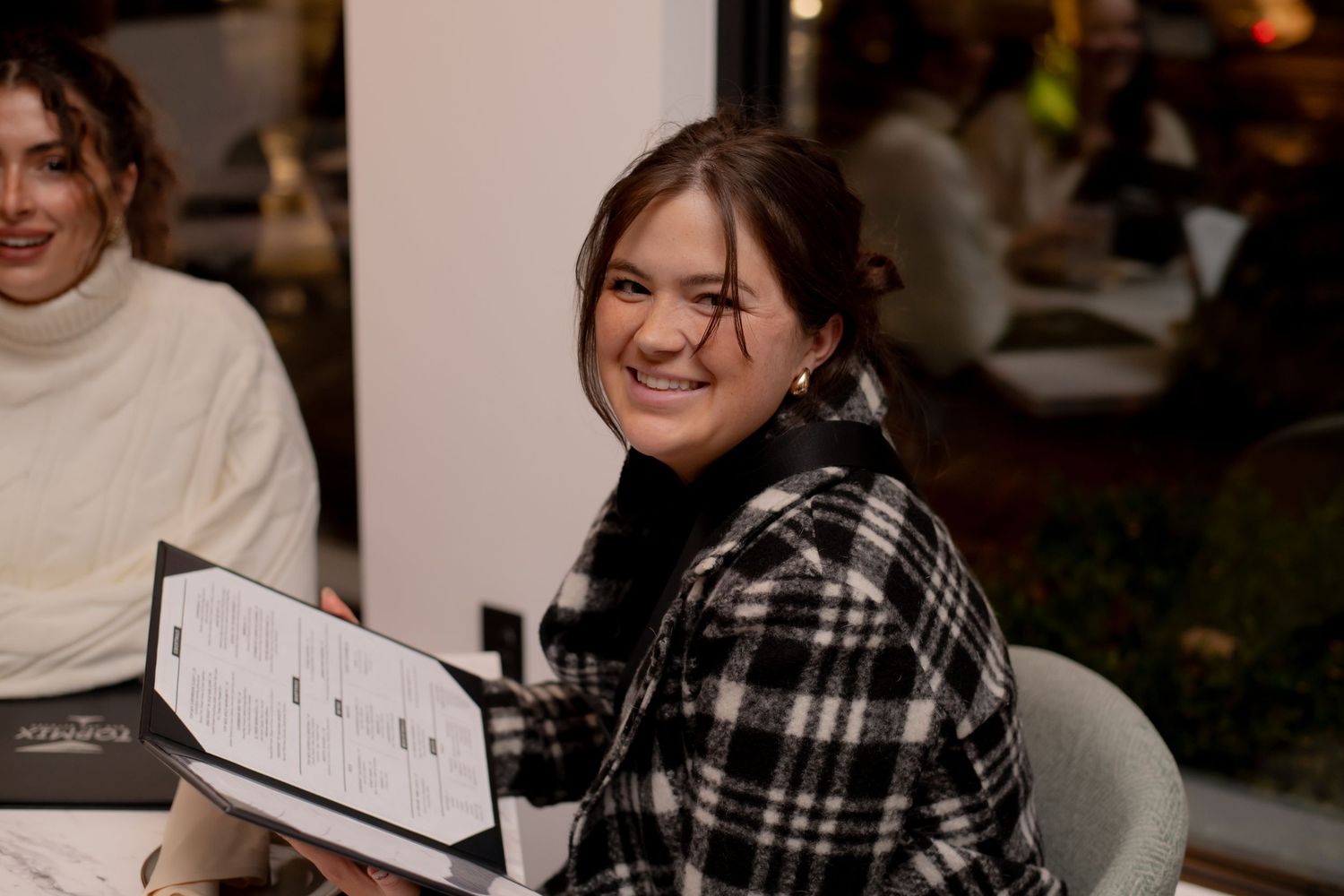 A young woman smiles while reviewing a menu at a stylish restaurant.