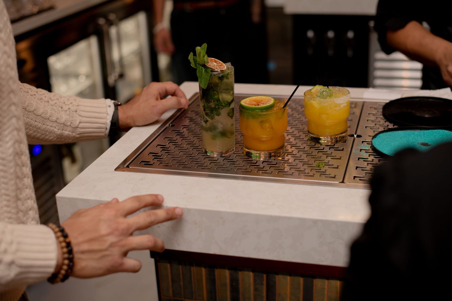Three colorful cocktails with garnishes are displayed on a bar counter at a restaurant.