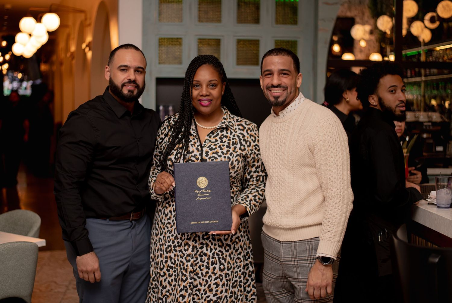 Three people smile and pose together holding a menu at an upscale restaurant event.