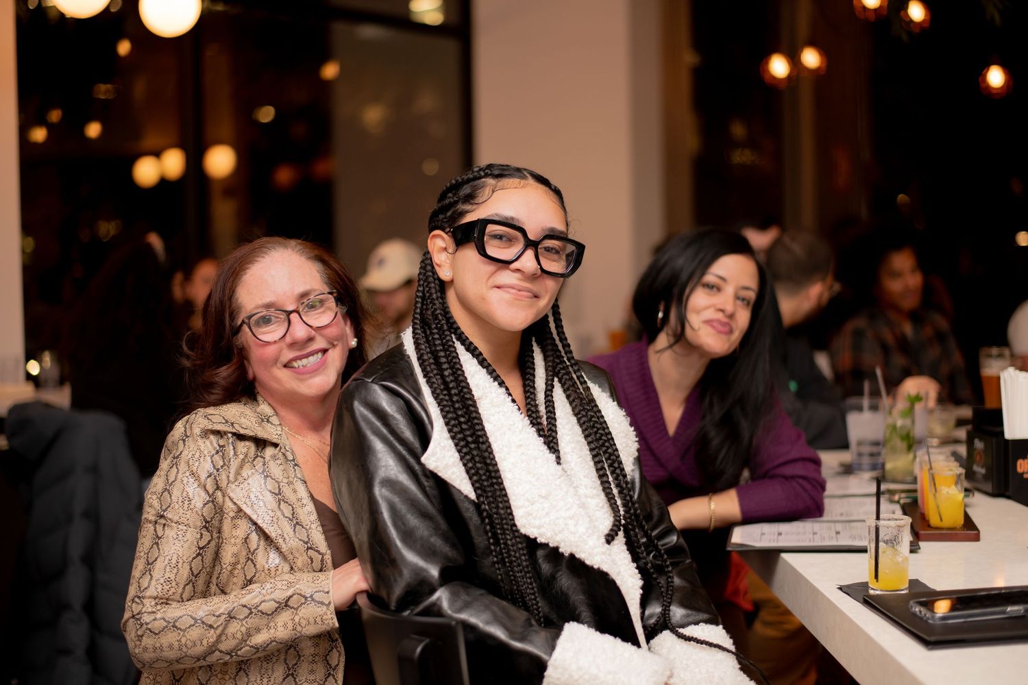 Two women smile together at a restaurant table during an evening social gathering event.