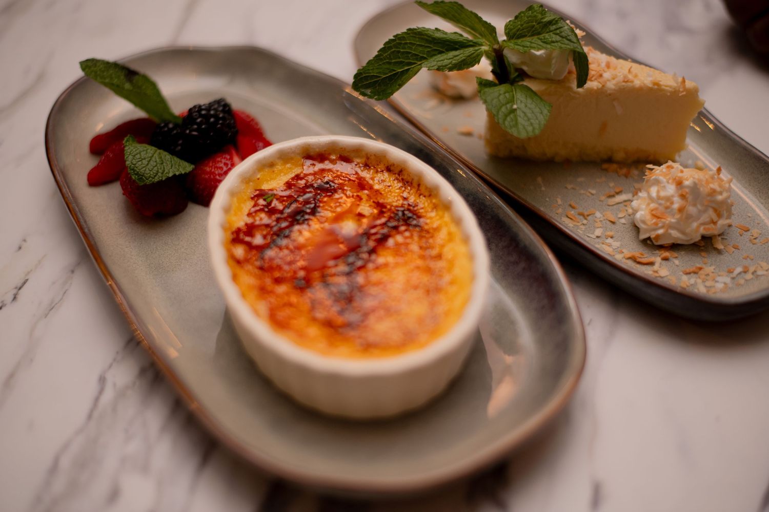 An elegant dessert plate with creme brulee, fresh berries, and cheesecake on a marble surface.