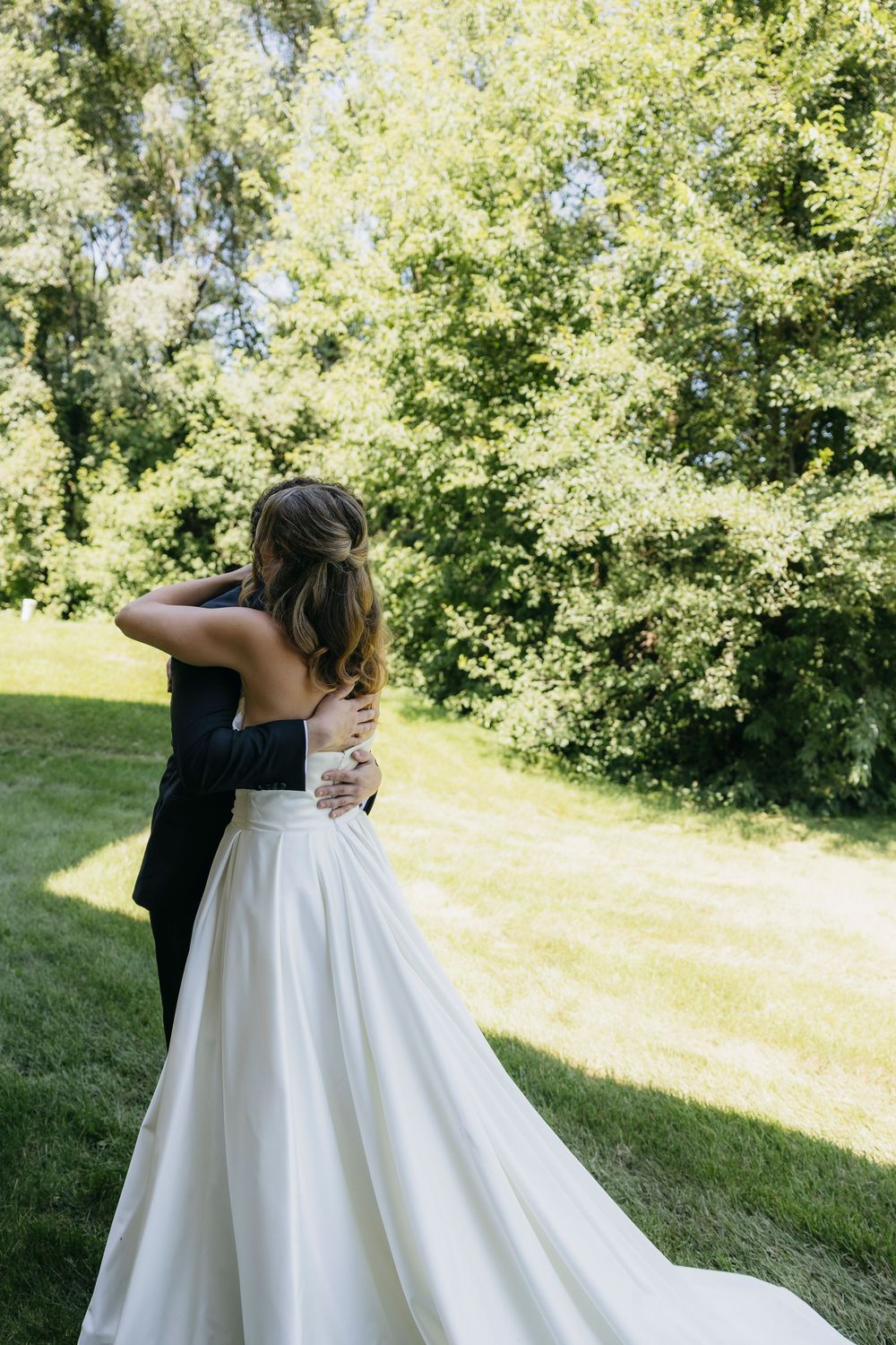 Bride and groom embracing outdoors in lush green garden, bride wearing elegant white strapless ball gown wedding dress after the first look
