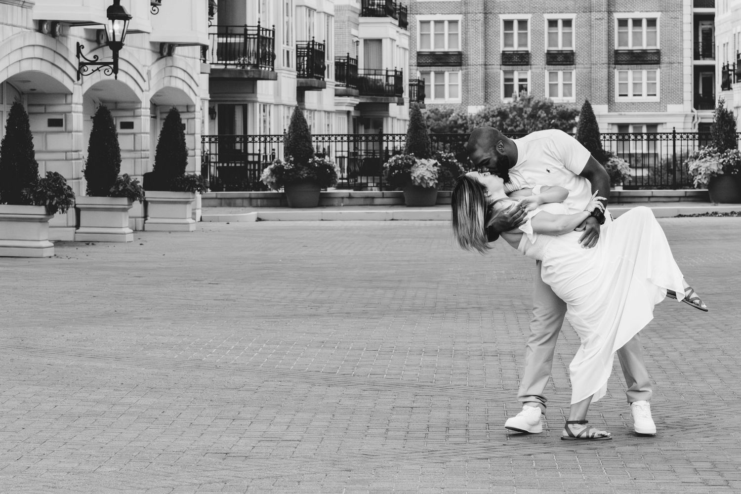 Couple sharing a romantic dip kiss in an urban plaza in black and white.