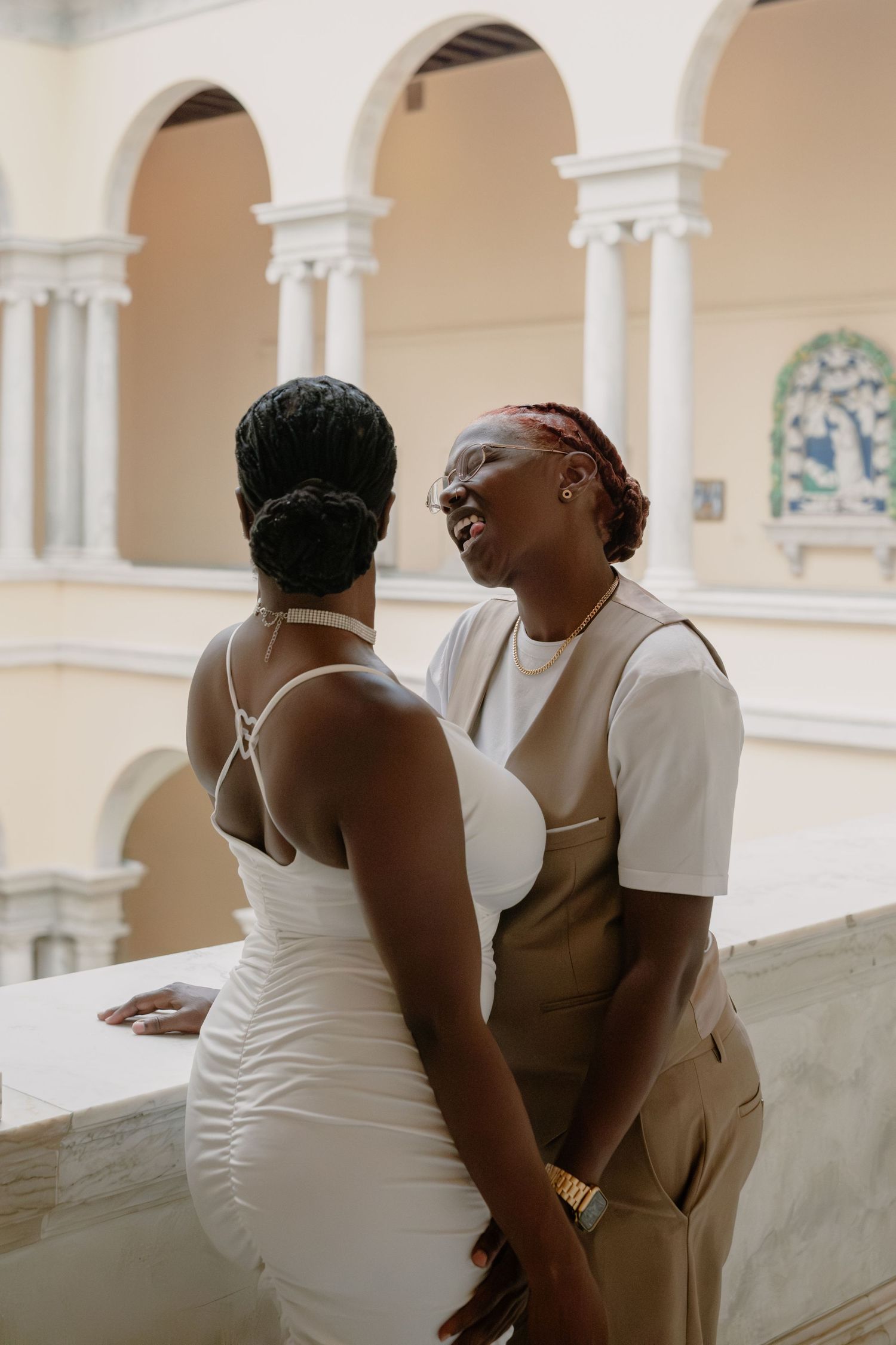 Two women share a joyful moment in a stunning classical architecture setting during a photoshoot.