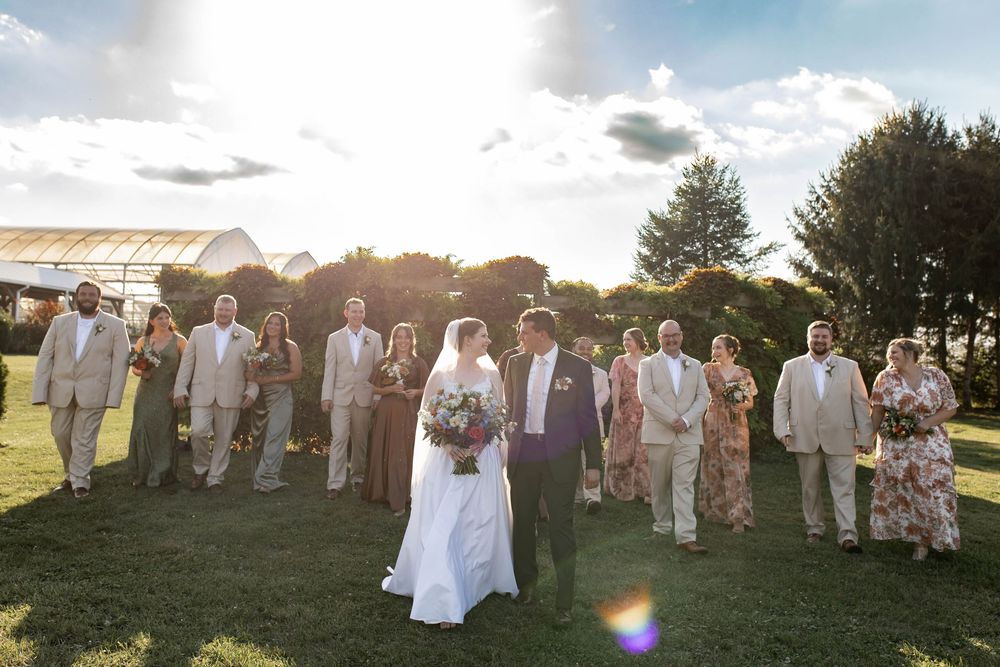 Wedding party walks together on green lawn at golden hour with bride and groom centered.