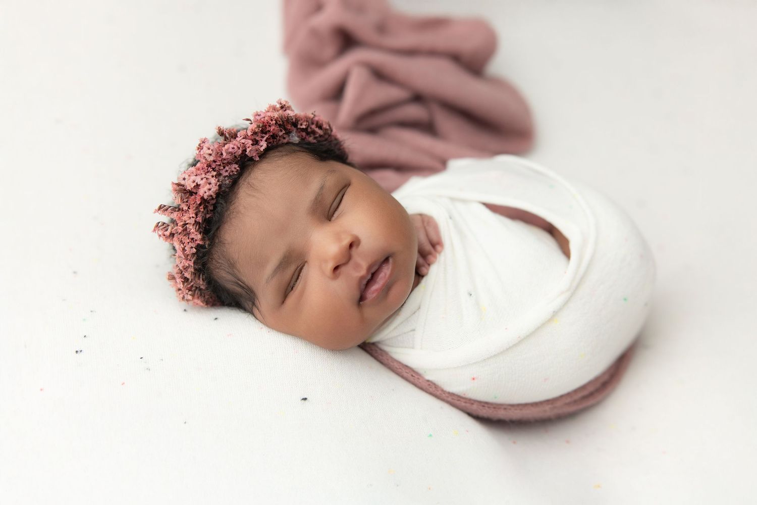 Newborn baby in teal hooded knit onesie with wooden buttons, sitting in a vintage metal bucket with soft teal blankets.