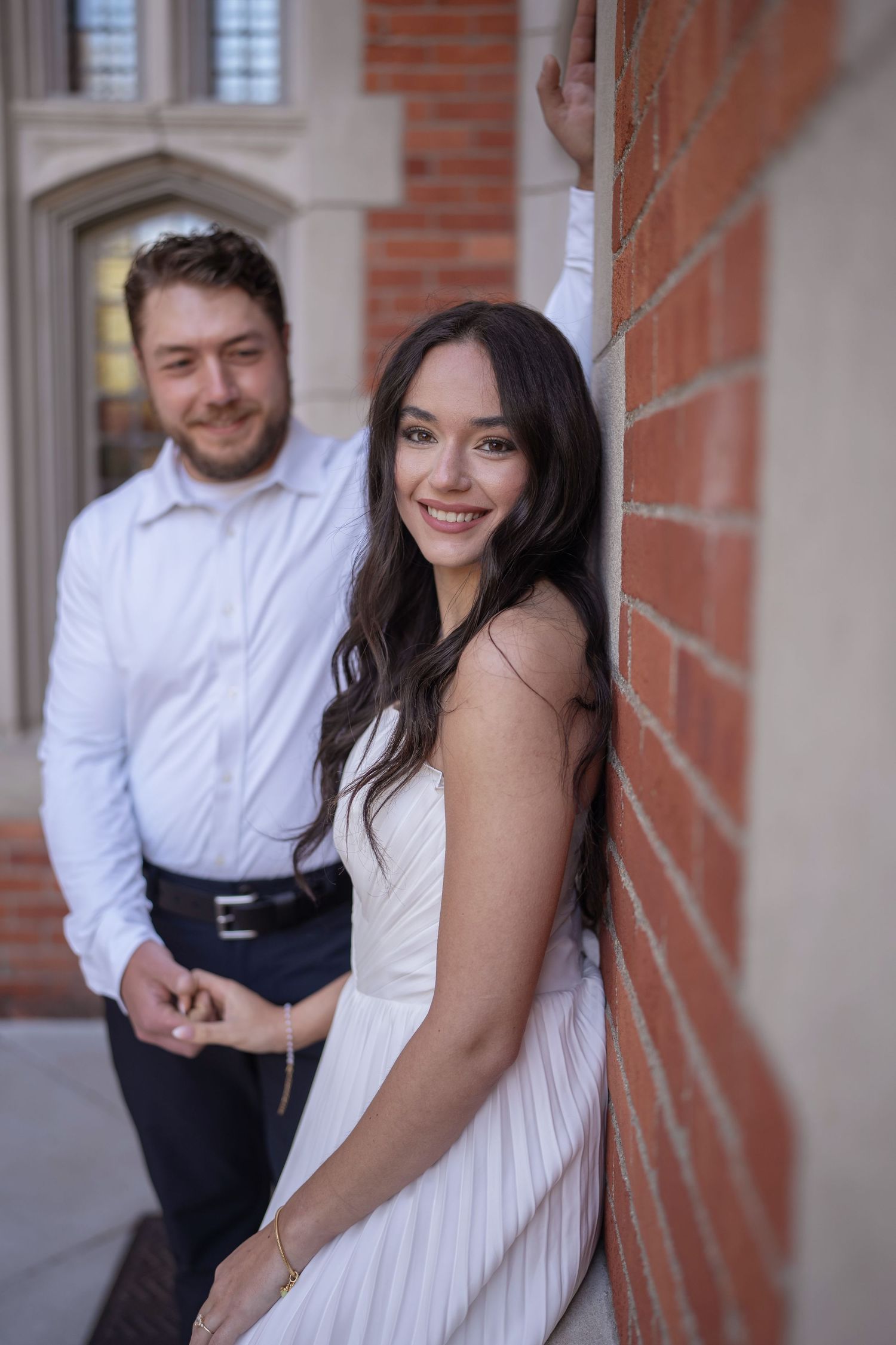 Smiling couple posing by a red brick wall, at Jeffrey Mansion for their Engagement Session