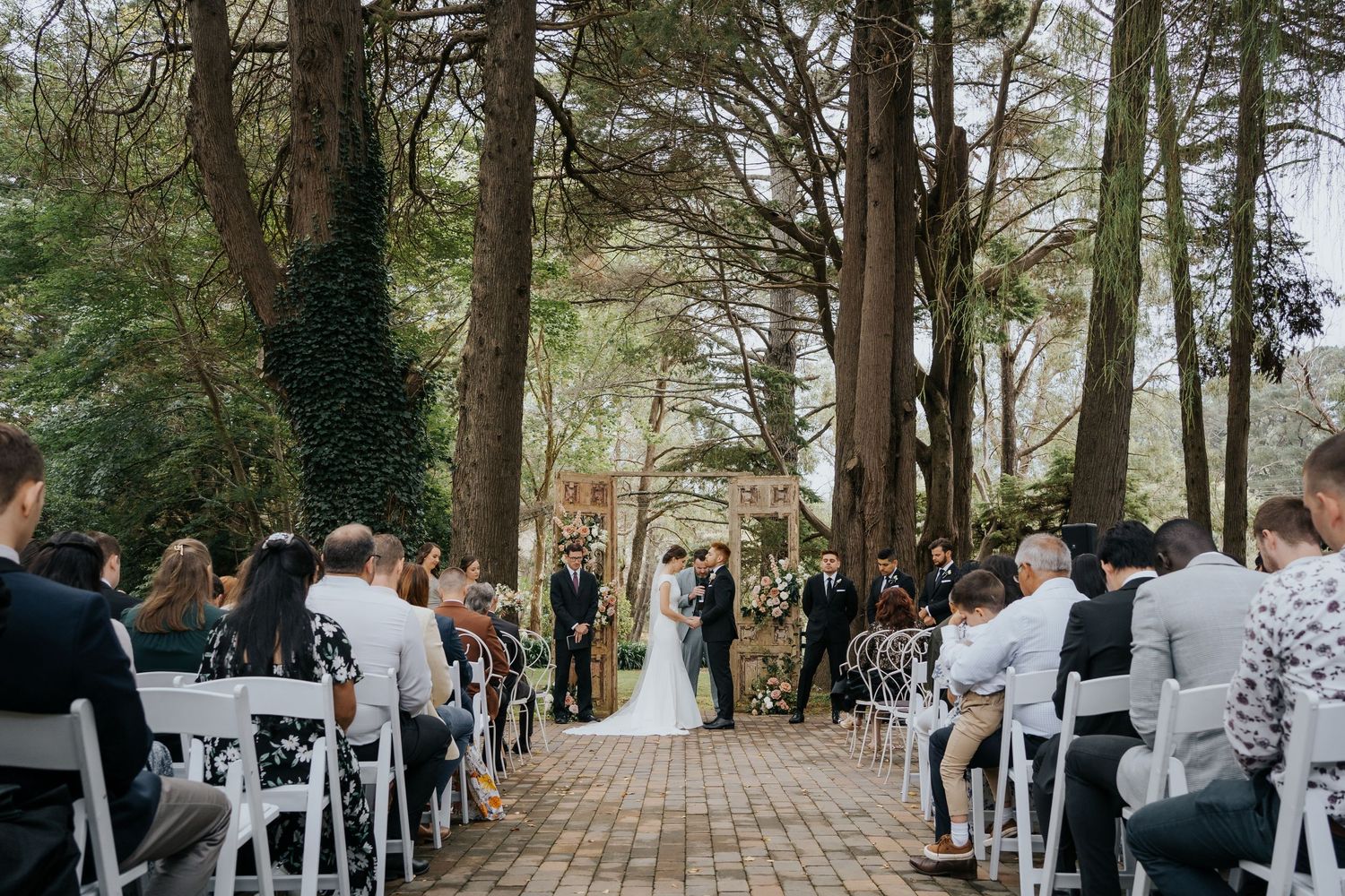 Bride and groom standing before a grand ivy-covered historic manor house on a cloudy day.