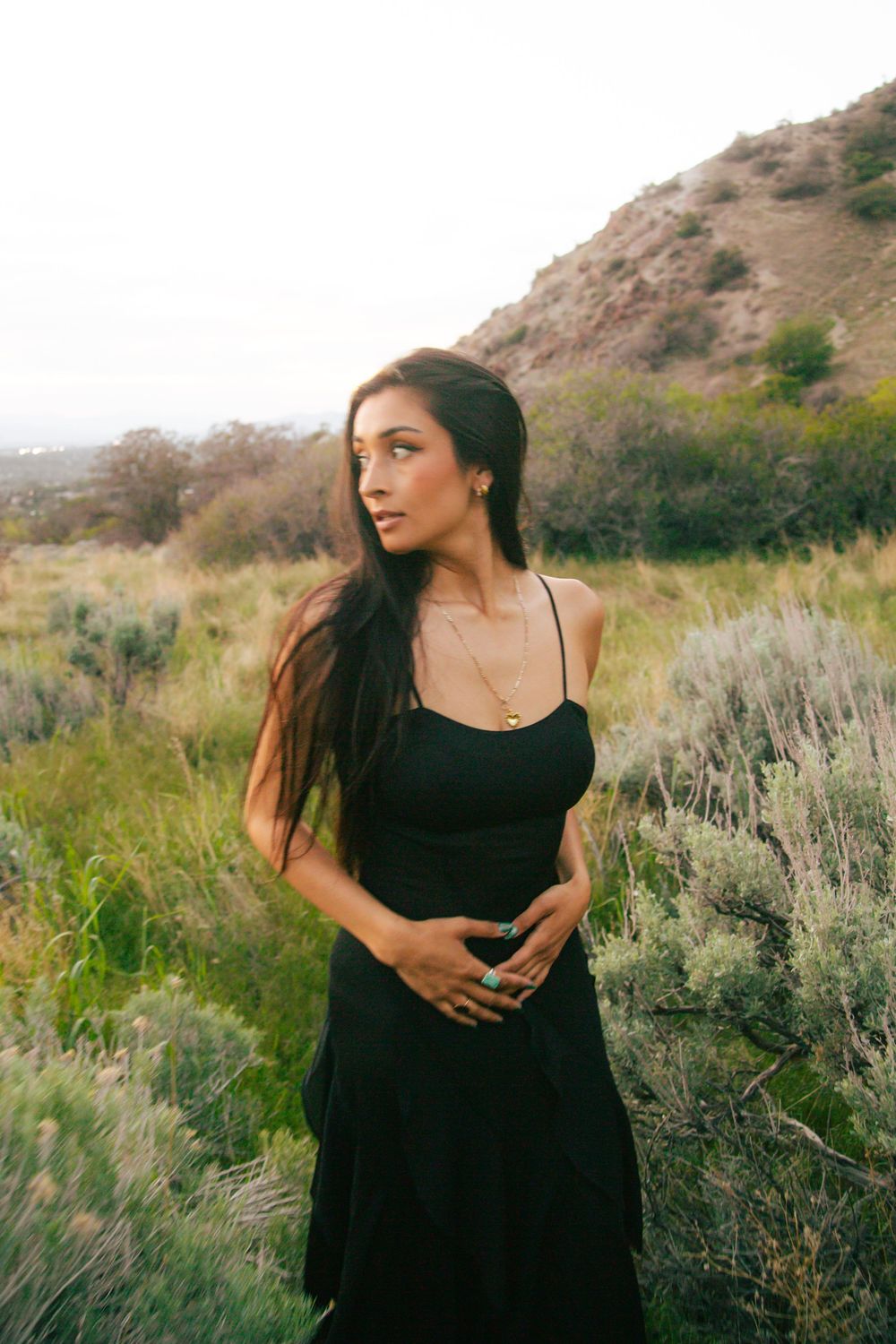 Brunette woman in black maxi dress with turquoise ring standing in sage brush hillside landscape.