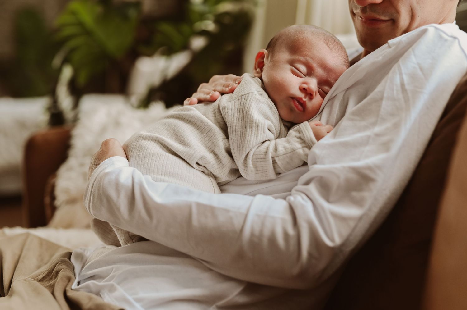 Newborn baby sleeping peacefully on parent's chest in warm cozy living room setting. Newborn lifestyle photography in Milwaukee, WI.