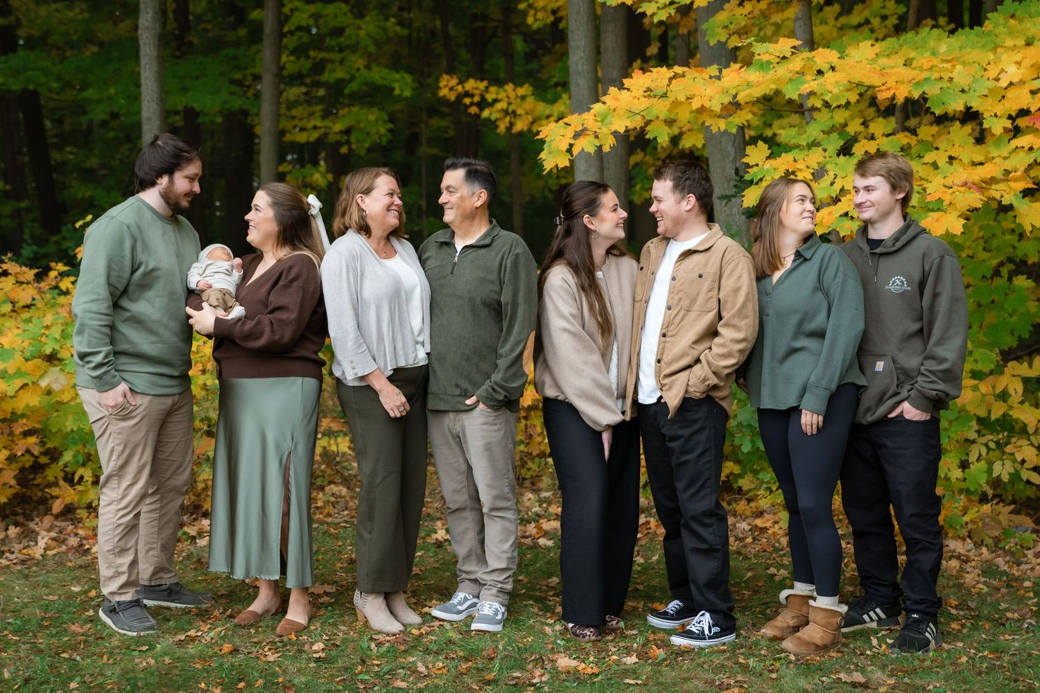 Family of five laughing together outdoors among vibrant autumn foliage in fall colors of yellow and orange.