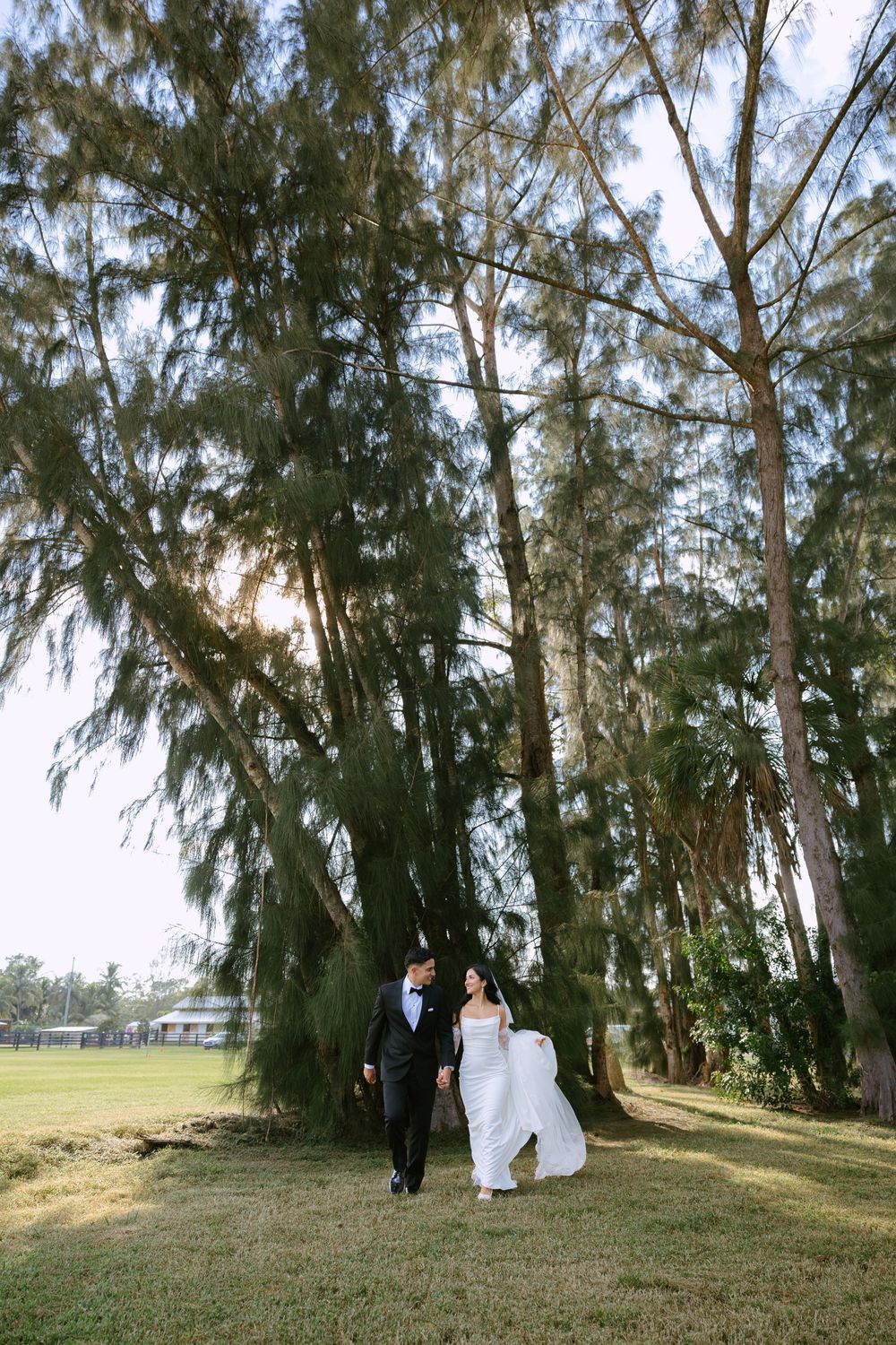 bride and groom in front of pine trees walking and holding hands at barn wedding at the ranch 22 in lake worth