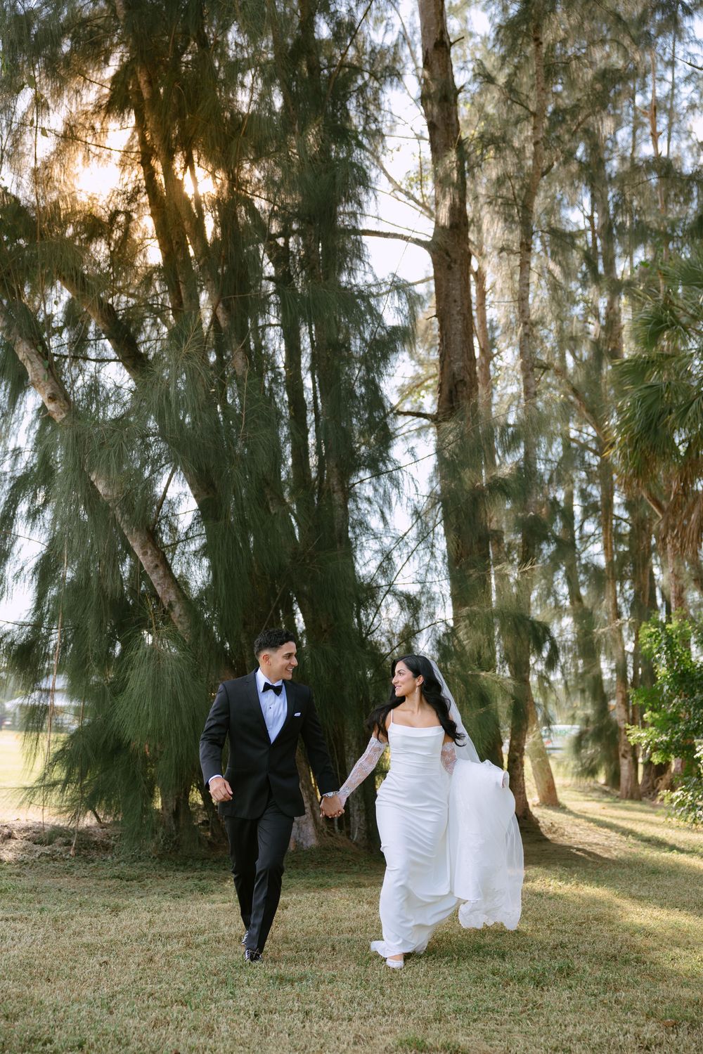 bride and groom in front of pine trees walking and holding hands at barn wedding at the ranch 22 in lake worth