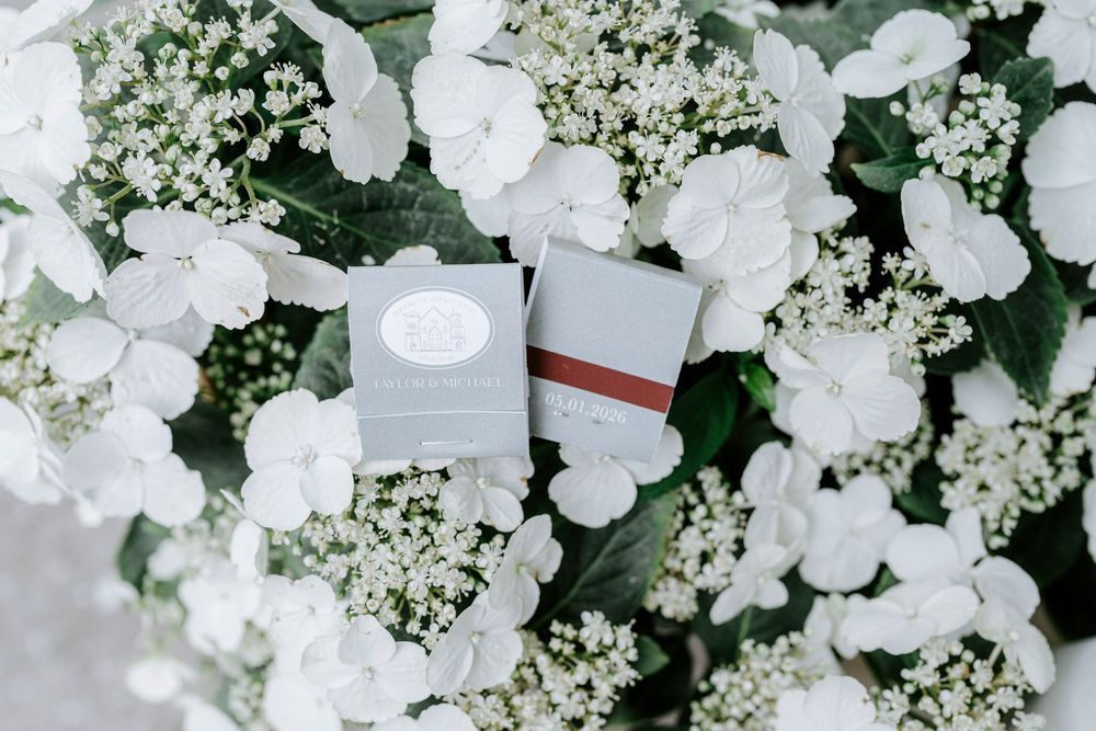 Two gray wedding invitation cards nestled among white hydrangea and baby's breath flowers.
