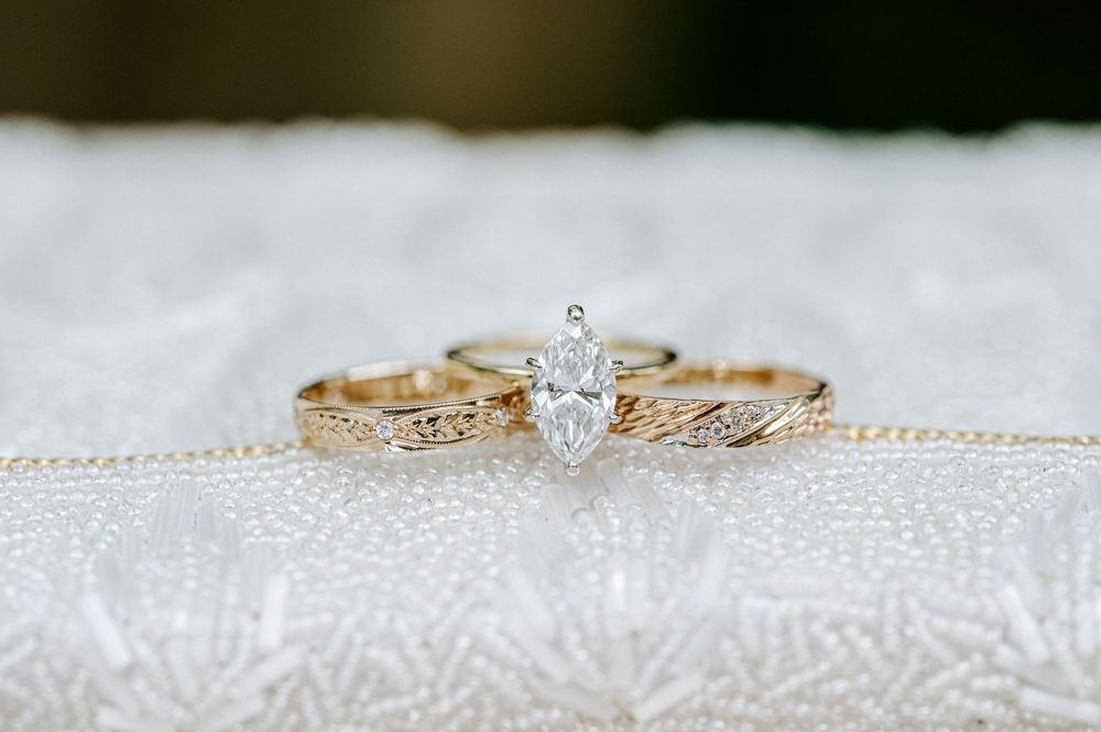 Gold marquise diamond engagement ring with matching engraved wedding bands displayed on white lace fabric.