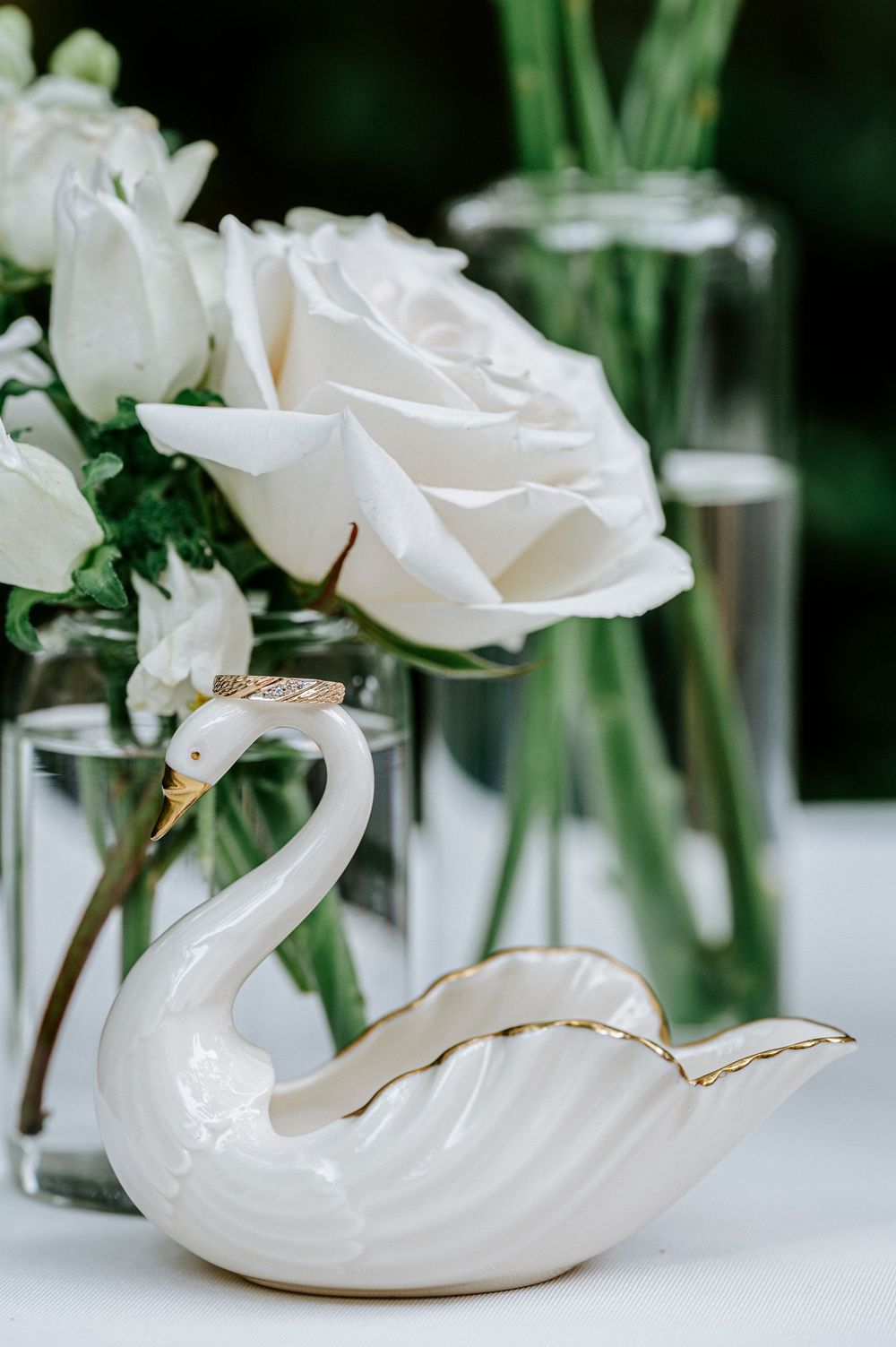 White ceramic swan figurine with gold trim beside white roses in glass vases at wedding reception.