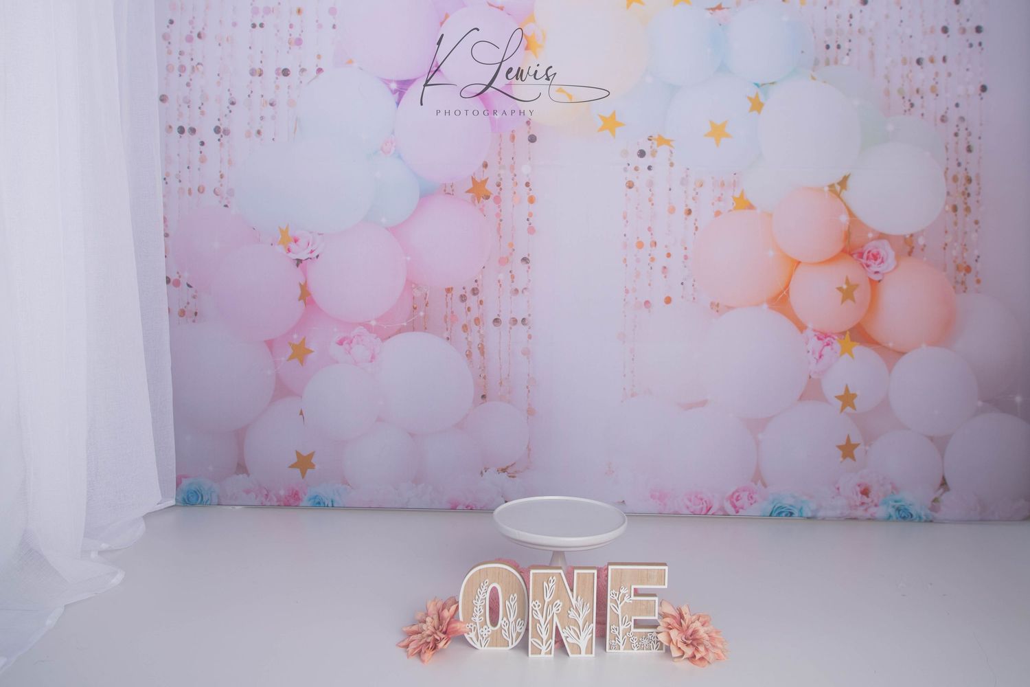 Pastel balloon backdrop with ONE letters and cake smash setup for a first birthday photo session.