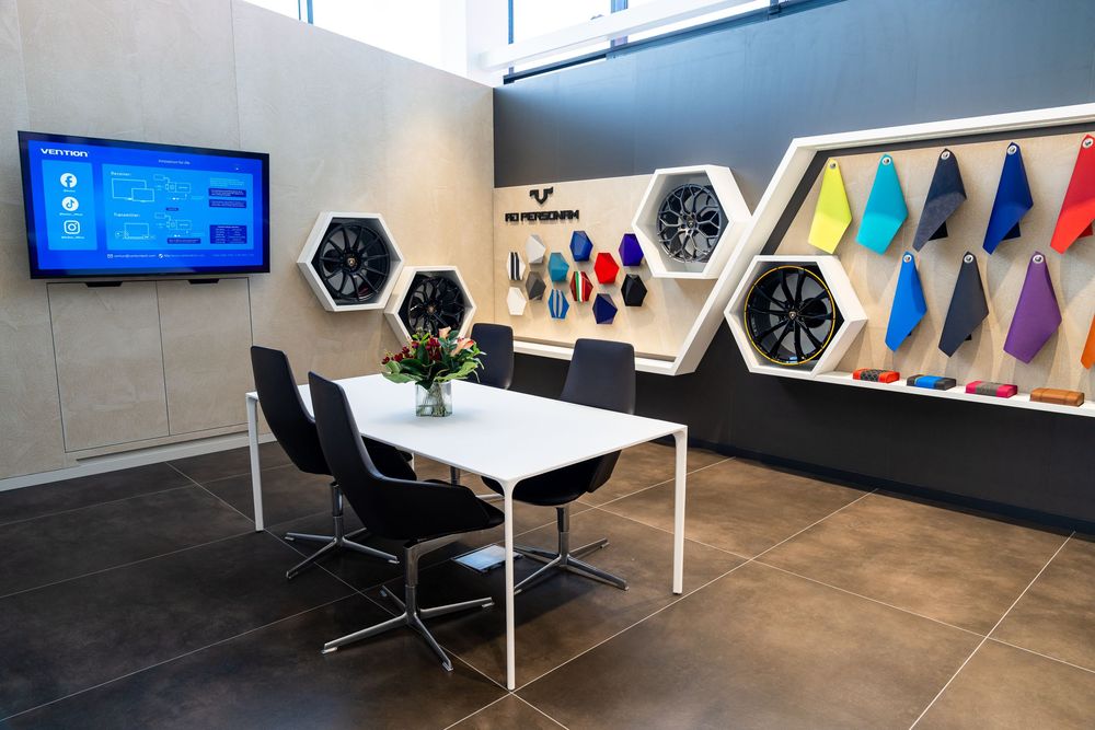Modern showroom with hexagonal wall displays featuring colorful panels, a white conference table, black chairs, and a wall-mounted TV.