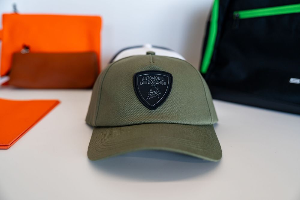 Olive green Lamborghini trucker cap with black shield logo patch on white surface.